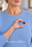 Broche fleur rose cerise portée sur un pull bleu clair avec un geste en demi-cœur